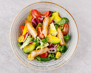 Salad with chicken, avocado, mango, cherry tomatoes, lettuce, onion removal, kumquat, on a gray background.
