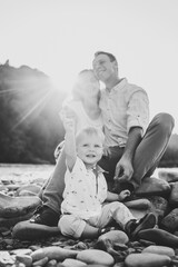 Happy family holiday in summer. Mother, father and baby son sitting on beach near lake. Fathers, mother, Children day. Spending time together. Mom, dad play with child at sunset. Black and white photo