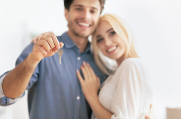 A happy couple stands together, the man holding up a set of keys, symbolizing their new home.
