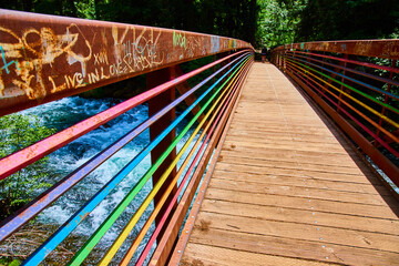 Colorful Rainbow Pedestrian Bridge Over Rushing River Eye-Level Perspective