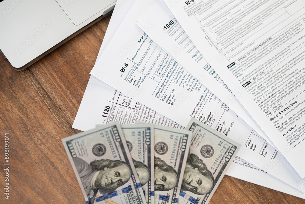 Poster assortment of tax forms near open laptop and dollar bills creating scene of organized chaos evoking 