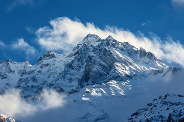 A snowy mountain peak with clouds covering the top, set against a bright blue sky