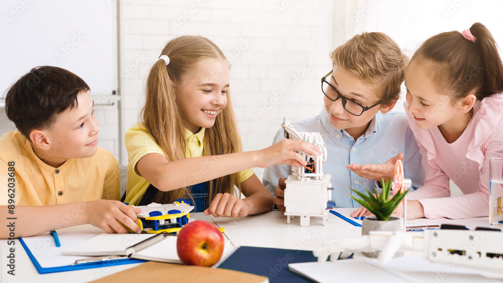 Aufkleber Four children, two boys and two girls, are working together on a robotics project in a classroom setting. They are all smiling and appear to be engaged in the task at hand