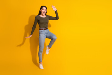 Full size photo of pretty teenager girl step wave hand hello wear trendy khaki outfit isolated on yellow color background