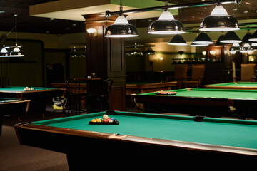 Part of spacious hall in modern bar or pub with two rows of green billiards tables with balls inside triangular racks and lamps above