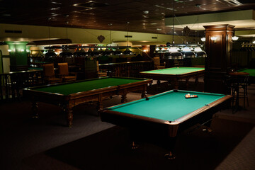 Several rows of tables for playing billiards with green tops standing in spacious hall of pub or club ready for leisure games