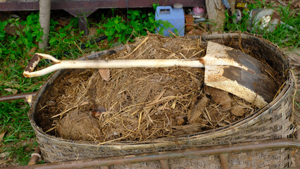 A rustic shovel resting on a pile of soil and straw in a woven basket, set against a backdrop of...