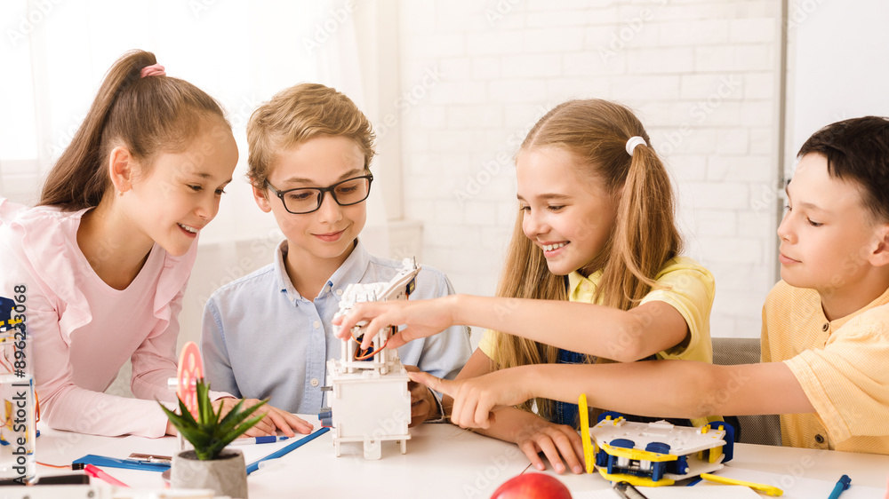 Poster This image shows four children working together on a STEM project in a classroom setting. The children appear to be focused and engaged in their work, and they are all smiling