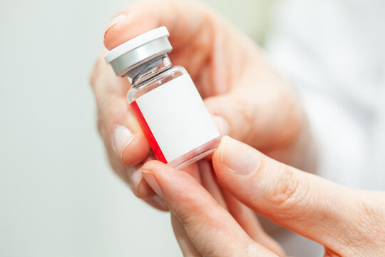Close up of doctor hands while holding a vial of an injectable liquid medicine.
