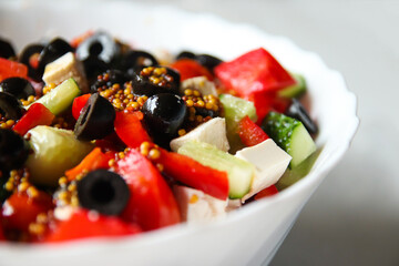 Summer salad. Classic Greek salad includes tomatoes, cucumbers, red pepper, onion, olives, oregano, and feta cheese. Fresh mixed vegetables are in a bowl, with black olives featured prominently
