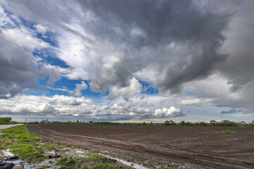 A plowed field stretches out before a dramatic sky, where dark, brooding storm clouds hang heavy...