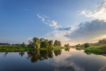 A calm river with trees on the banks and a cloudy sky in the background