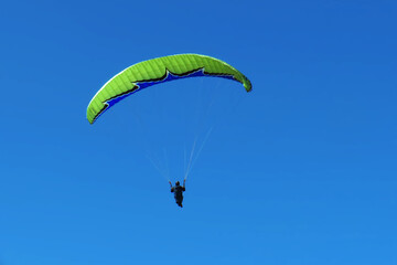 A man with a paraglider in front of a blue sky.