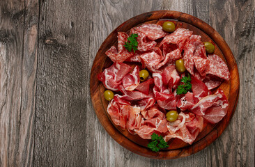 Assortment , sliced meat appetizer, prosciutto, salami and ham, with olives, on a wooden board,...