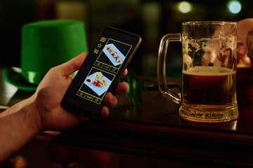Hand of young unrecognizable man holding mobile phone with photos of sushi rolls on screen while having beer by bar counter