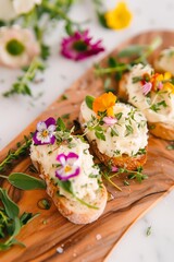 wooden board with open sandwiches with creamy butter spread, topped with fresh herbs, edible flowers, and drizzled with honey