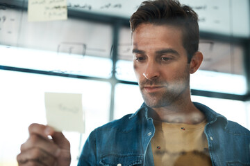 Business, man and glass with sticky notes in office for brainstorming, information and solution of project goal. Male person, reading and idea on paper for reminder, timeline and agenda schedule - Powered by Adobe