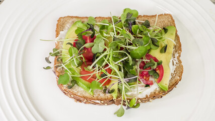 Avocado, tomato, and microgreen open-faced sandwich on whole grain toast