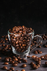 Coffee beans in a transparent mug on a dark background. Natural light