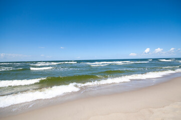 Sandy beach and sea waves by sunny day
