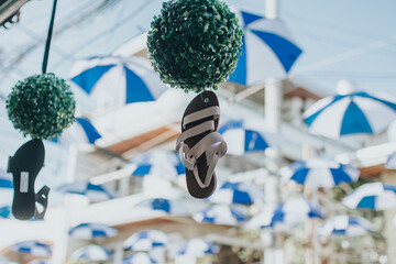 Hanging flip-flop ornament suspended from green topiary sphere under blue and white umbrella canopy...