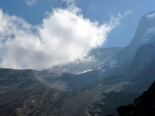 A view of the picturesque slope of a large mountain under a blue sky and a white cloud. Beautiful summer landscape