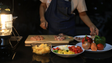 A woman prepares ingredients and prepares BBQ. Grilling for the party in the night. A woman is getting ingredients ready and grilling BBQ for a party at night.