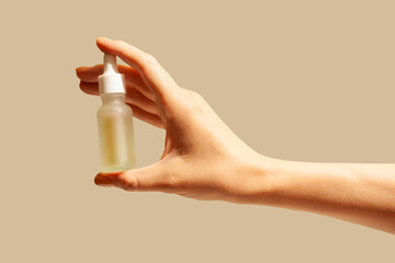 Cosmetic serum or ampoule essence in woman hand isolated on beige background
