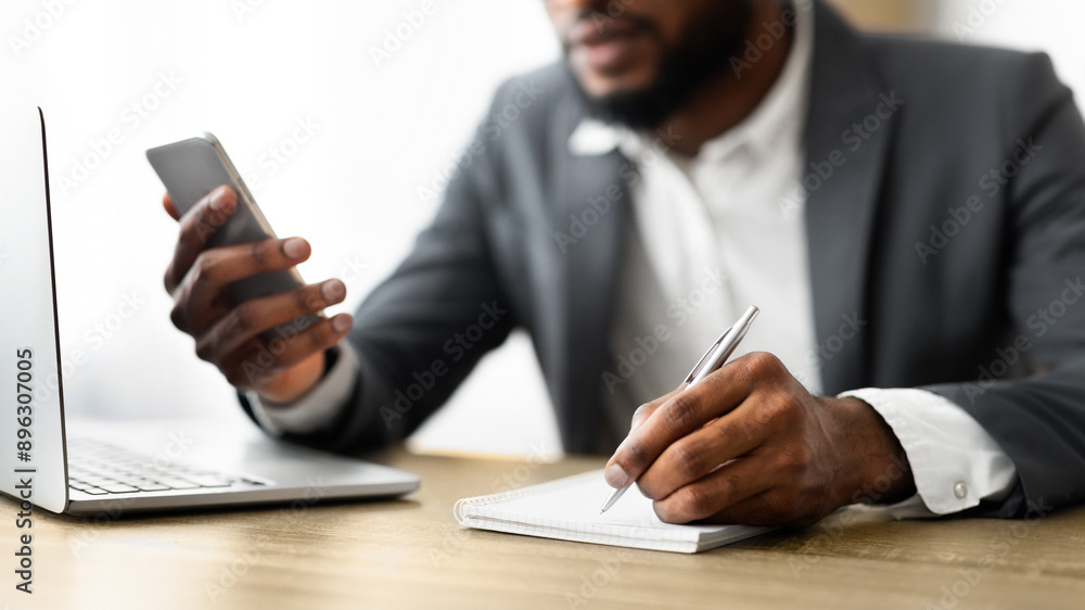 Poster african american employer using smartphone and taking notes while working in office, selective focus