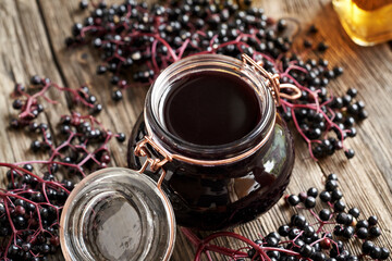A jar of black elder syrup with fresh elderberries