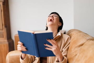 Woman Laughing While Reading Book on Couch