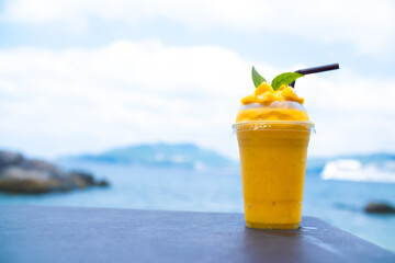 Smoothie made from fresh mango fruits against the backdrop of a seascape. Fruit and yoghurt ice cream decorated with leaves. Glass of tropical dessert close-up.