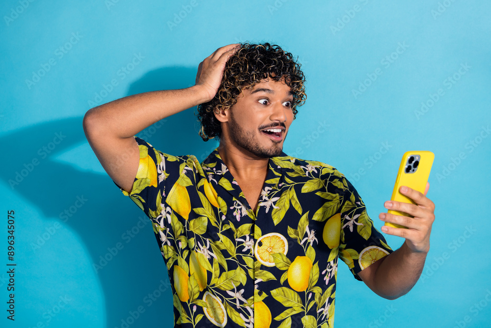 Wall mural photo of overjoyed crazy man with wavy hairstyle dressed print shirt look at smartphone arm on head 