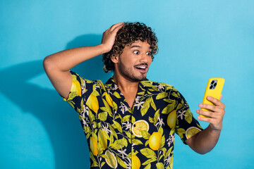Photo of overjoyed crazy man with wavy hairstyle dressed print shirt look at smartphone arm on head...