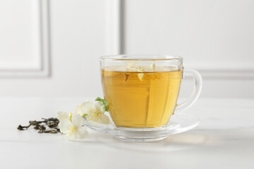 Aromatic jasmine tea in cup, flowers and dry leaves on white marble table