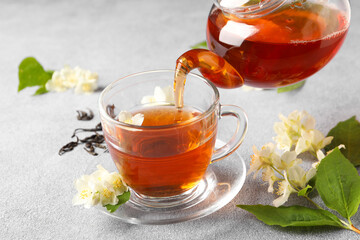 Pouring hot jasmine tea into cup on light grey table, closeup