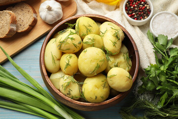 Tasty young boiled potatoes with dill in bowl served on light blue wooden table, flat lay