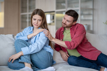 Smiling careful husband calms upset vulnerable wife on home couch, talk after quarrel and peace....