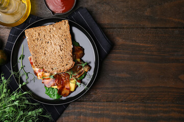 Tasty sandwich with bacon and microgreens served on wooden table, flat lay. Space for text