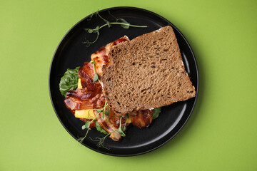 Tasty sandwich with bacon and microgreens on green table, top view