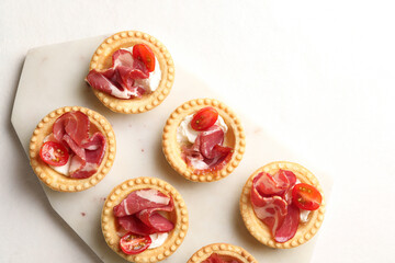 Delicious canapes with jamon, cream cheese and cherry tomatoes on white table, top view