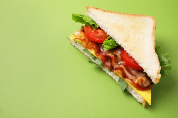 Delicious sandwich with fried bacon on green background, closeup. Space for text