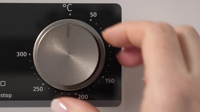 Woman adjusting modern white oven in kitchen. Female hand pushing and turning knobs on oven control panel. Closeup