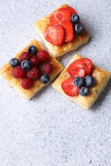 Tasty puff pastries with berries on light grey table, flat lay. Space for text