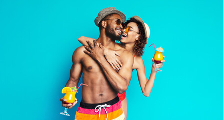 African American happy couple, both wearing sunglasses and summer clothing, smiles and laughs while holding refreshing cocktails