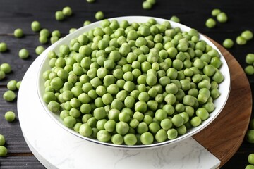 Fresh green peas in bowl on black wooden table, closeup