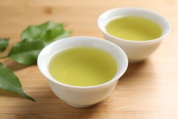 Refreshing green tea in cups and leaves on wooden table, closeup
