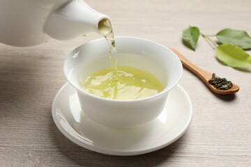 Pouring refreshing green tea into cup at wooden table, closeup