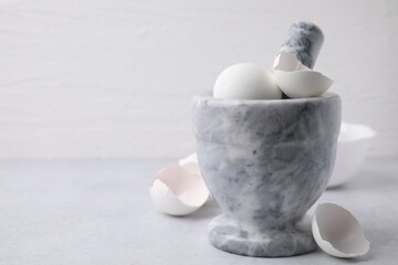 Broken eggshells, mortar and pestle on grey table, closeup. Space for text