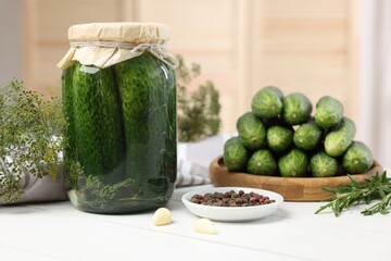 Pickled cucumbers in jar, dill and peppercorns on white wooden table, closeup